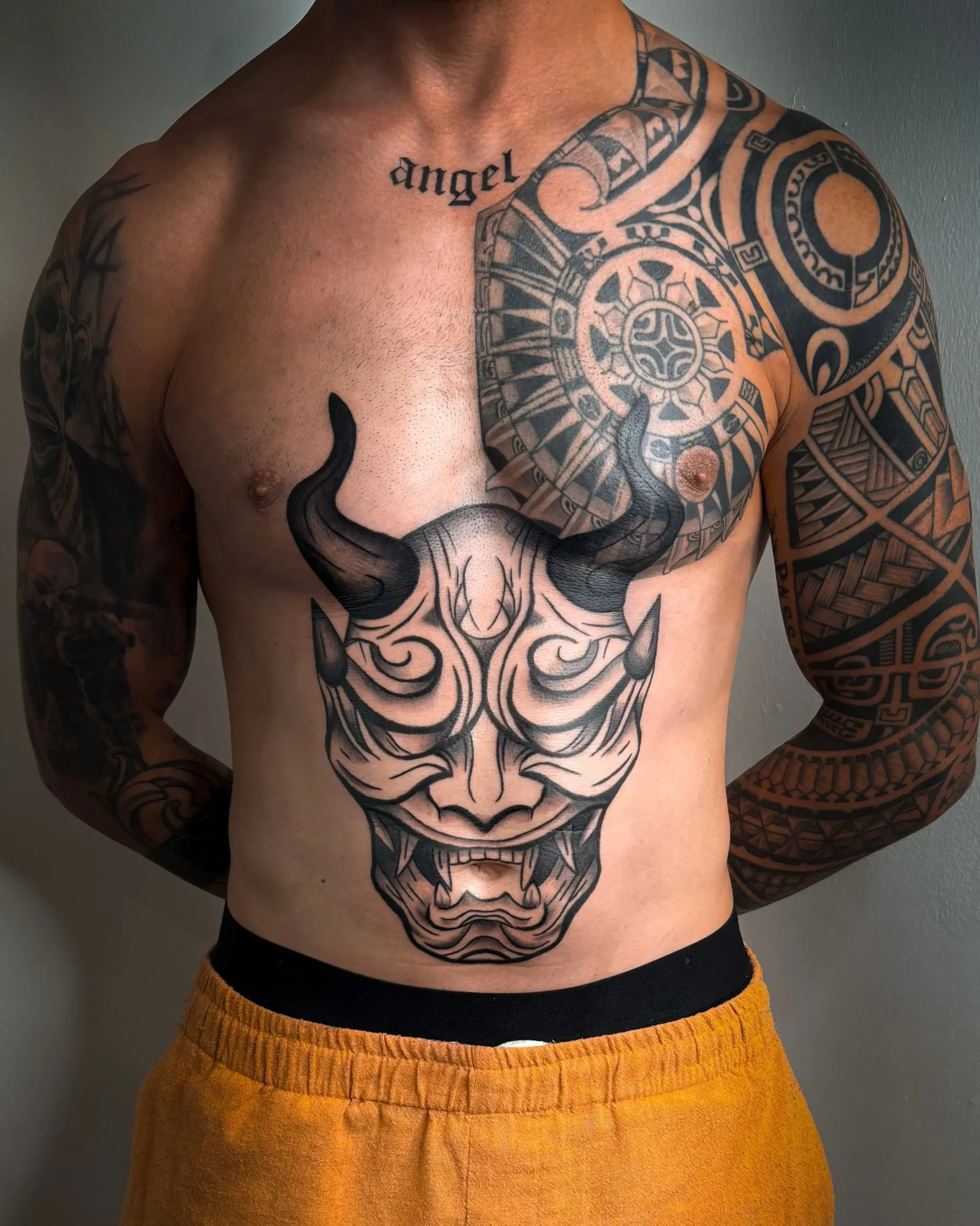 Large Japanese Hannya mask tattoo on stomach with tribal shoulder sleeve, professional blackwork at Walk In Tattoo Budapest.