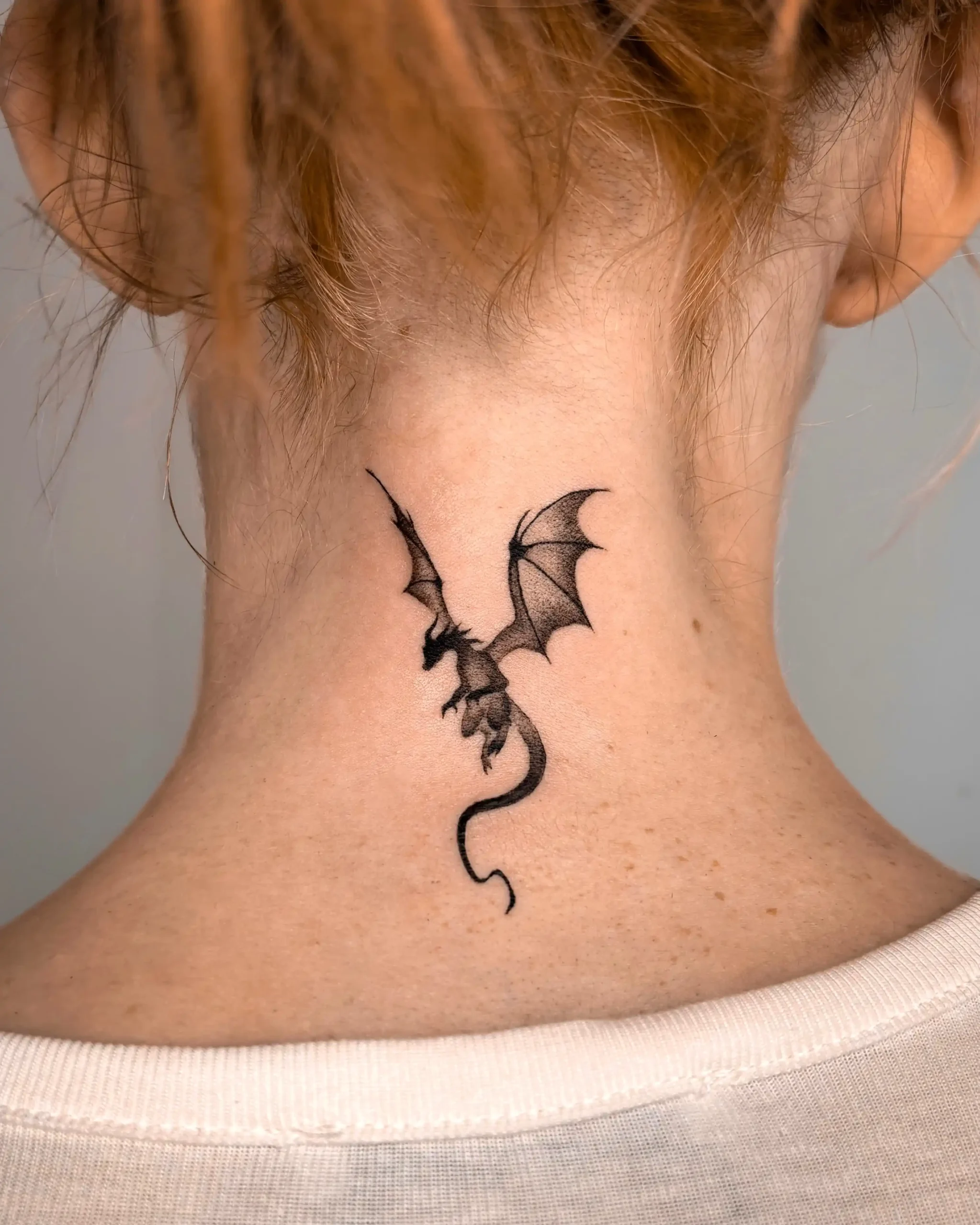 Small black ink dragon tattoo on the back of the neck, elegant fantasy design created at Walk In Tattoo Budapest.