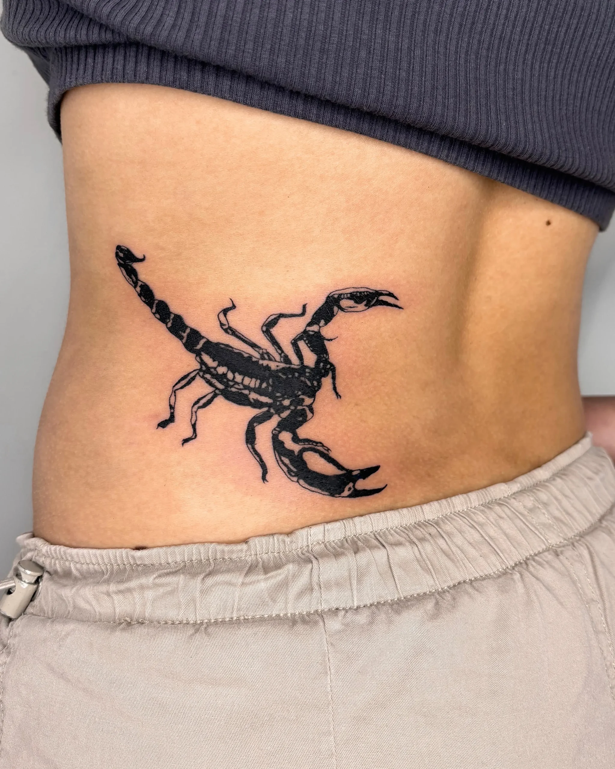 High-contrast blackwork scorpion tattoo on the lower back and waist - Walk In Tattoo Budapest