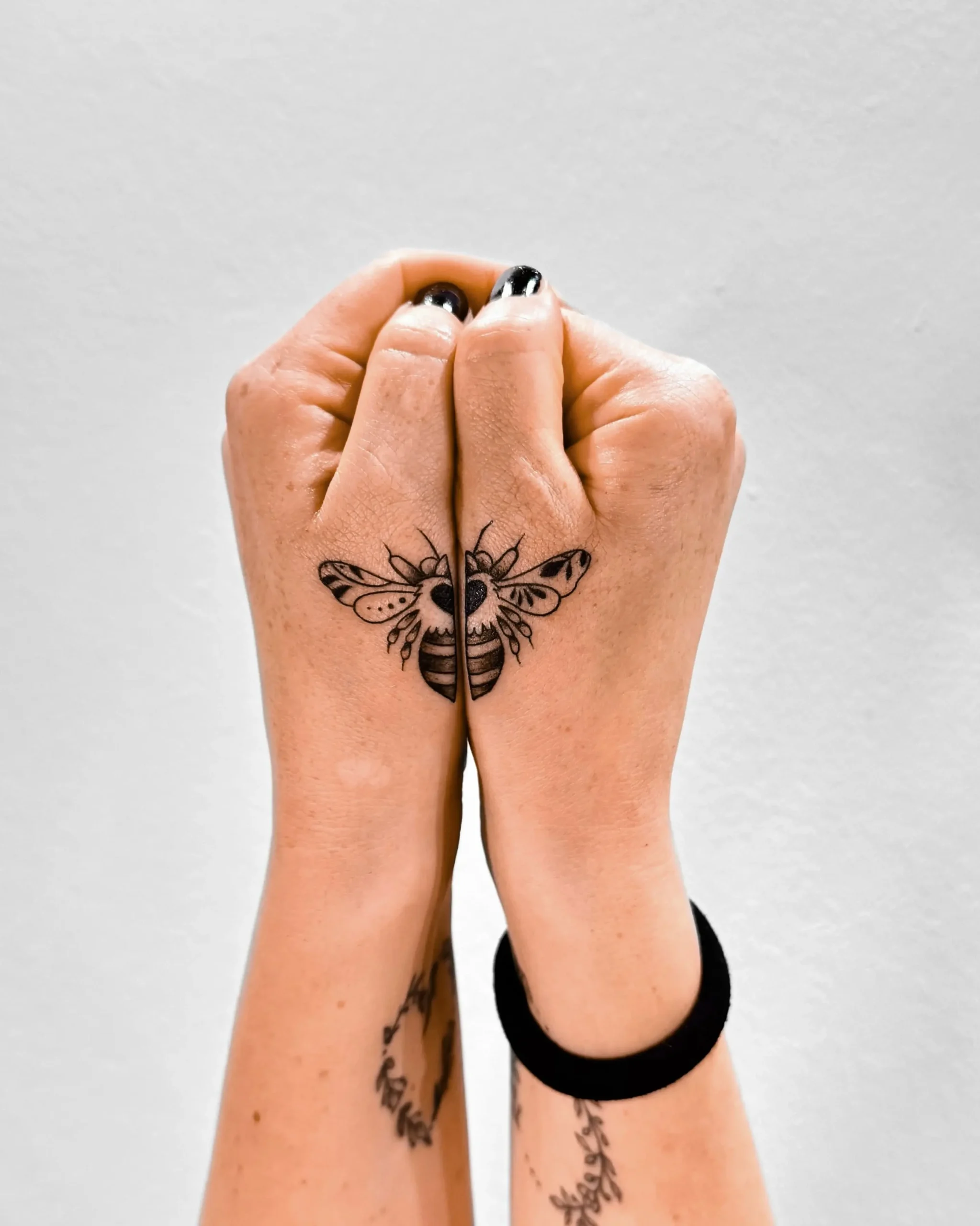 Small bee tattoo split across both hands, creative symmetry blackwork style, Walk In Tattoo Budapest studio.