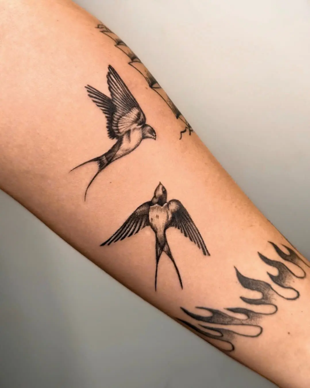 Pair of traditional fine line swallow tattoos on forearm with flame details - Walk In Tattoo Budapest