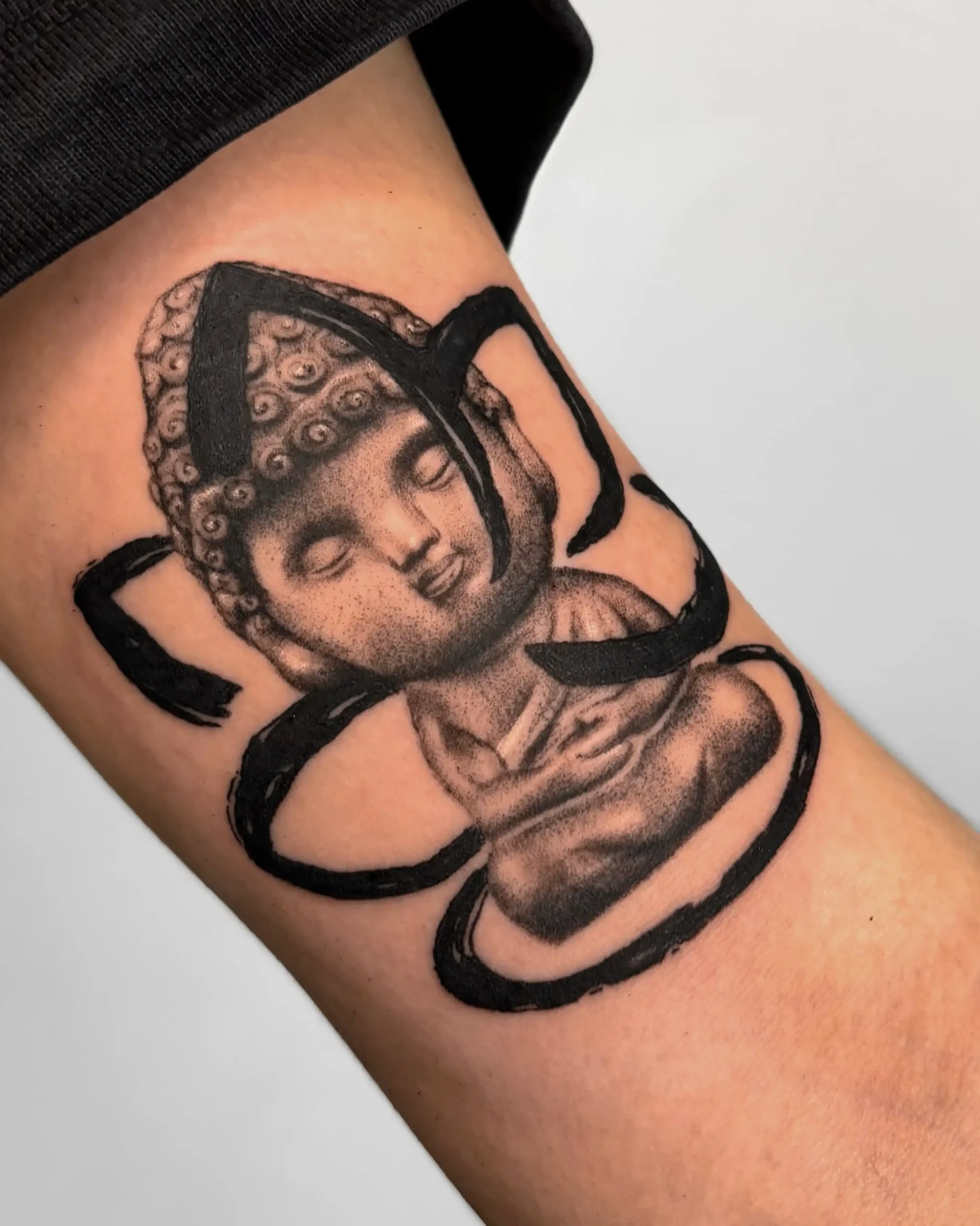 Small Buddha tattoo with black abstract calligraphy on forearm, Walk In Tattoo Budapest. Small Buddha tattoo with black abstract calligraphy on forearm, Walk In Tattoo Budapest.