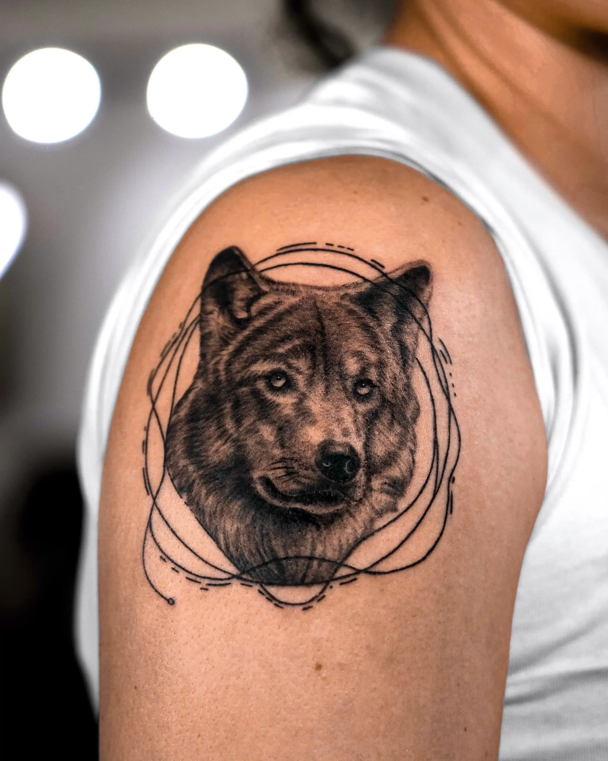 Realistic wolf portrait tattoo on upper arm with abstract geometric lines, Walk In Tattoo Budapest studio.