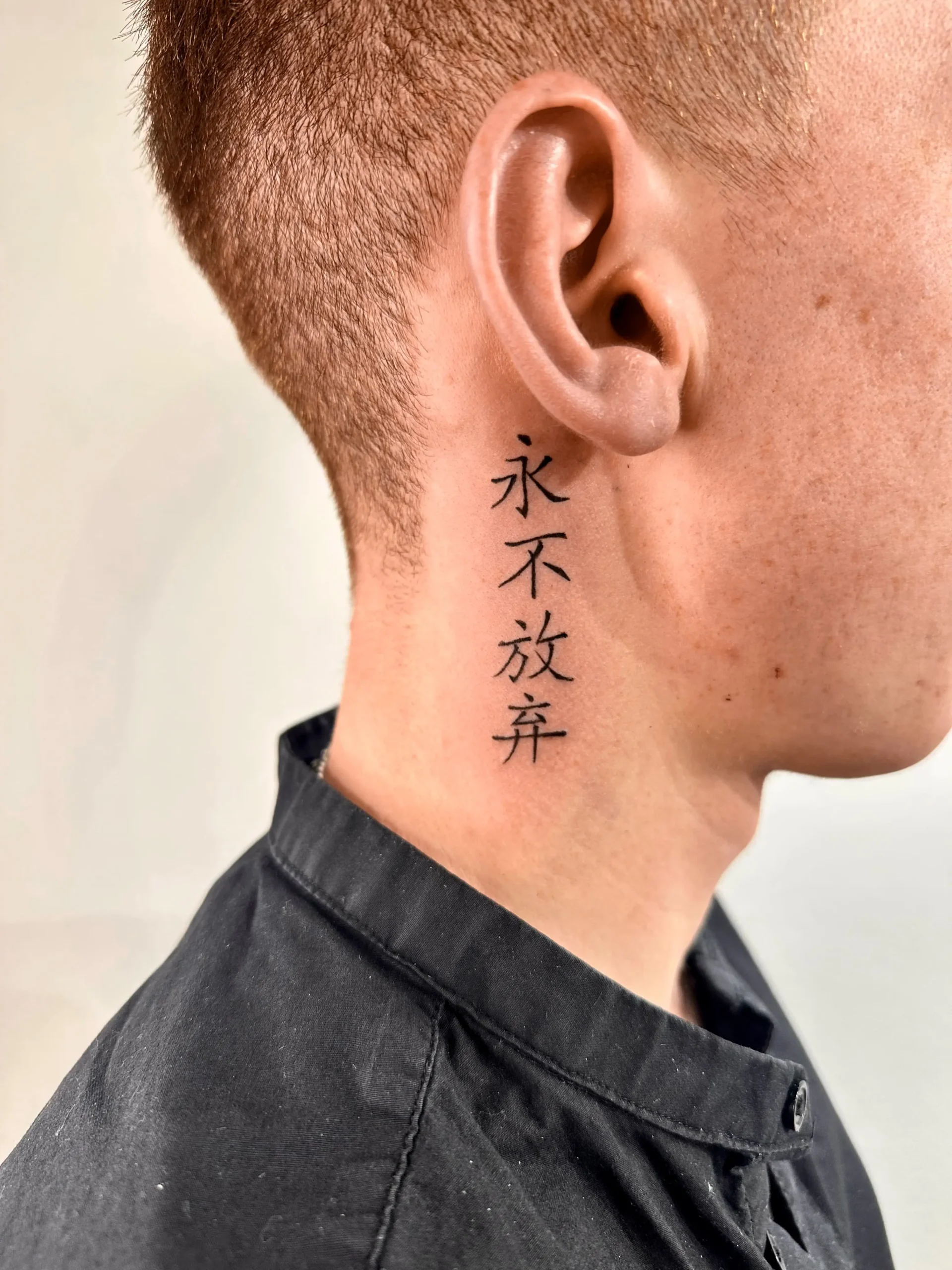 Minimalist Chinese calligraphy neck tattoo with vertical black ink characters - Walk In Tattoo Budapest