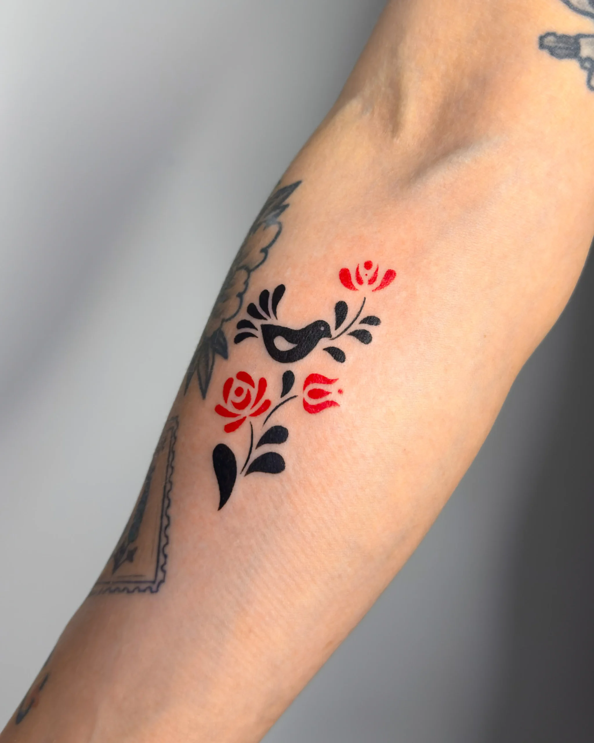 Folk art style tattoo of a black bird and red flowers on a forearm