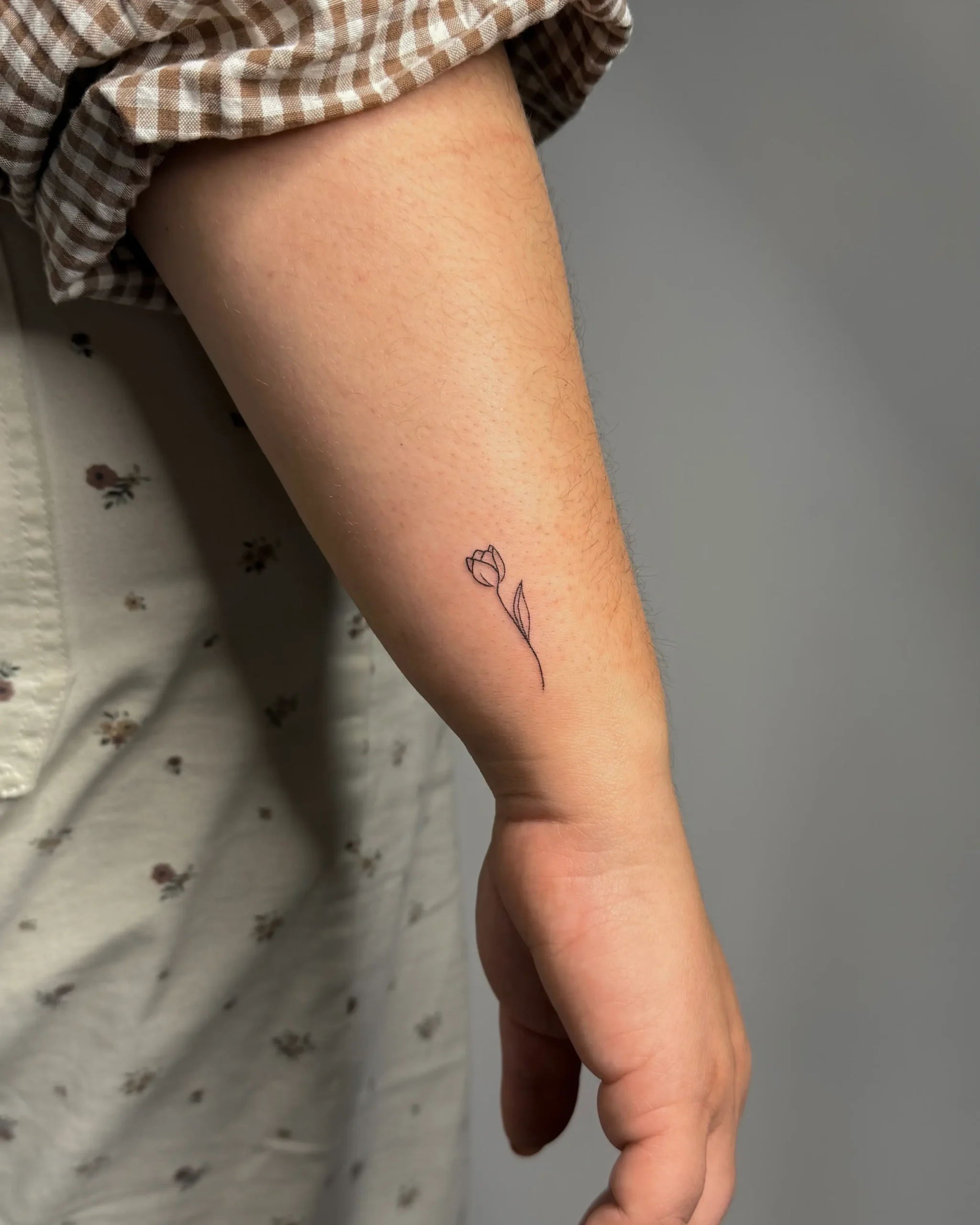 Minimalist fineline tulip tattoo on the inner forearm
