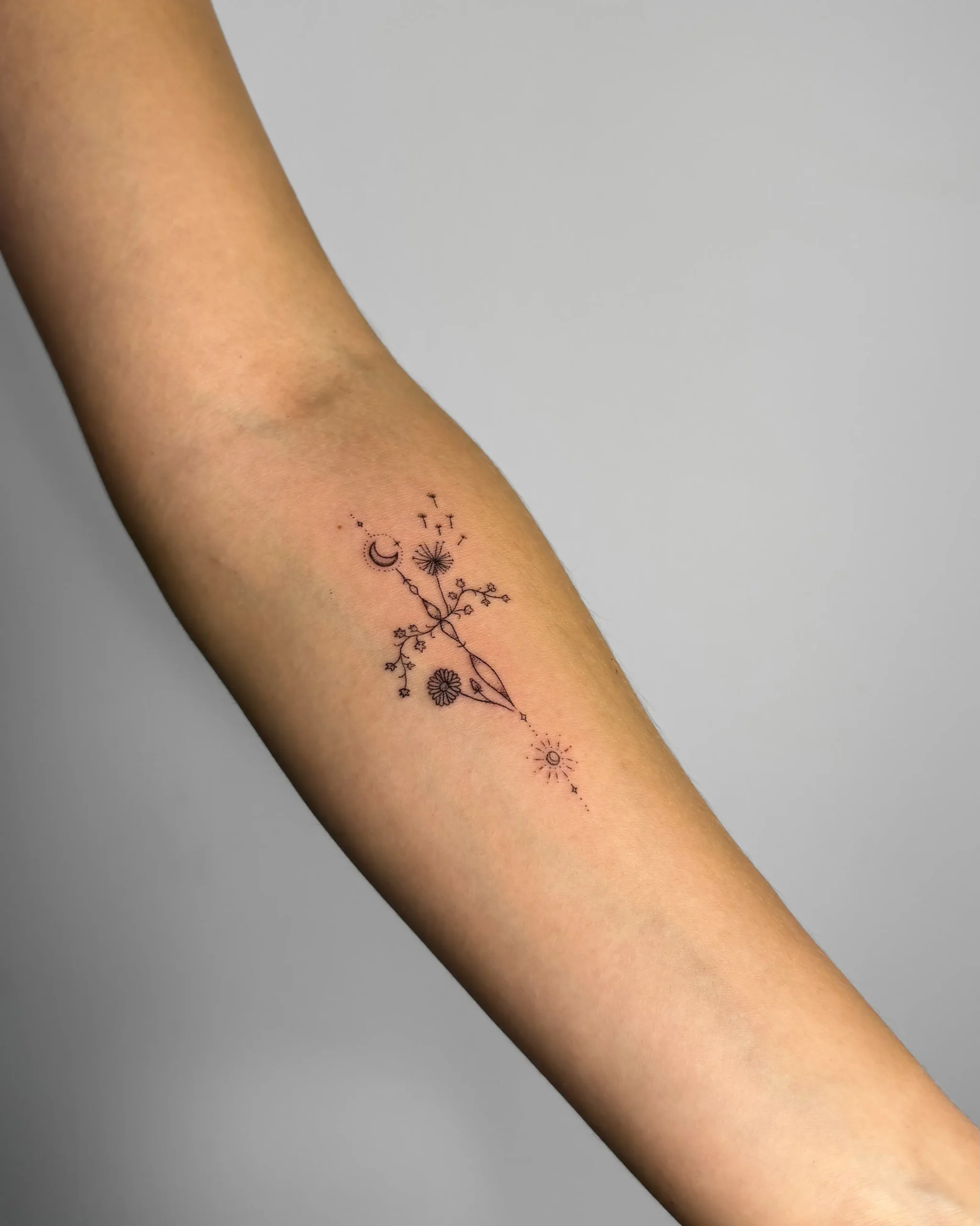 Celestial fineline tattoo with moon, sun, and wildflowers on the inner arm